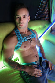 Man with tattoos wearing a blue aqua harness on a green couch. Made By Breedwell